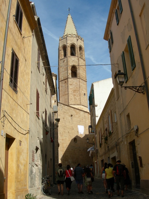 Da una vietta di Alghero, ci si dirige verso la chiesa. In alto svetta il campanile che va ad immergersi nel cielo azzurro!
